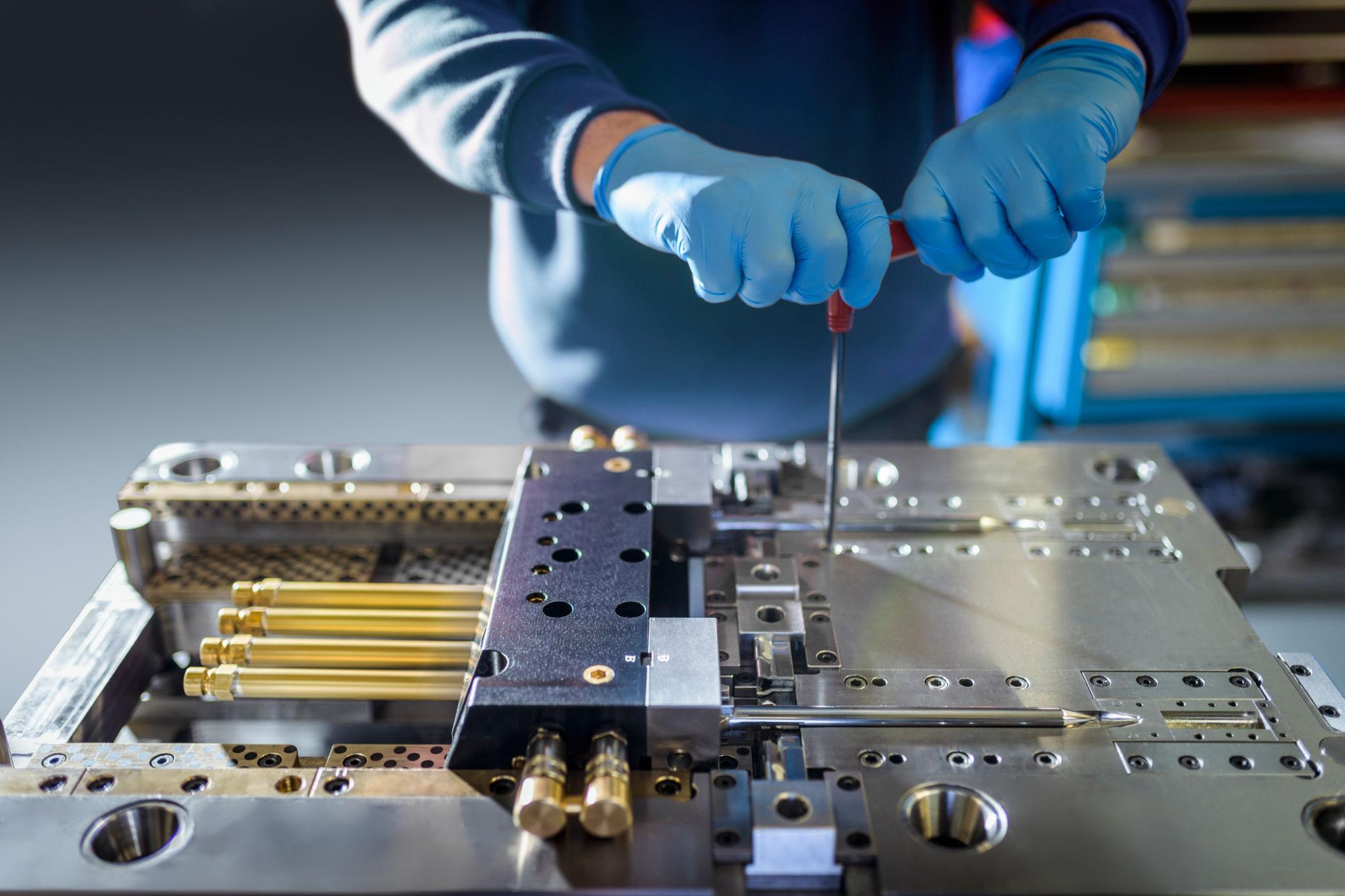 Engineer working on plastic injection mould in precision engineering factory, mid section, close up.