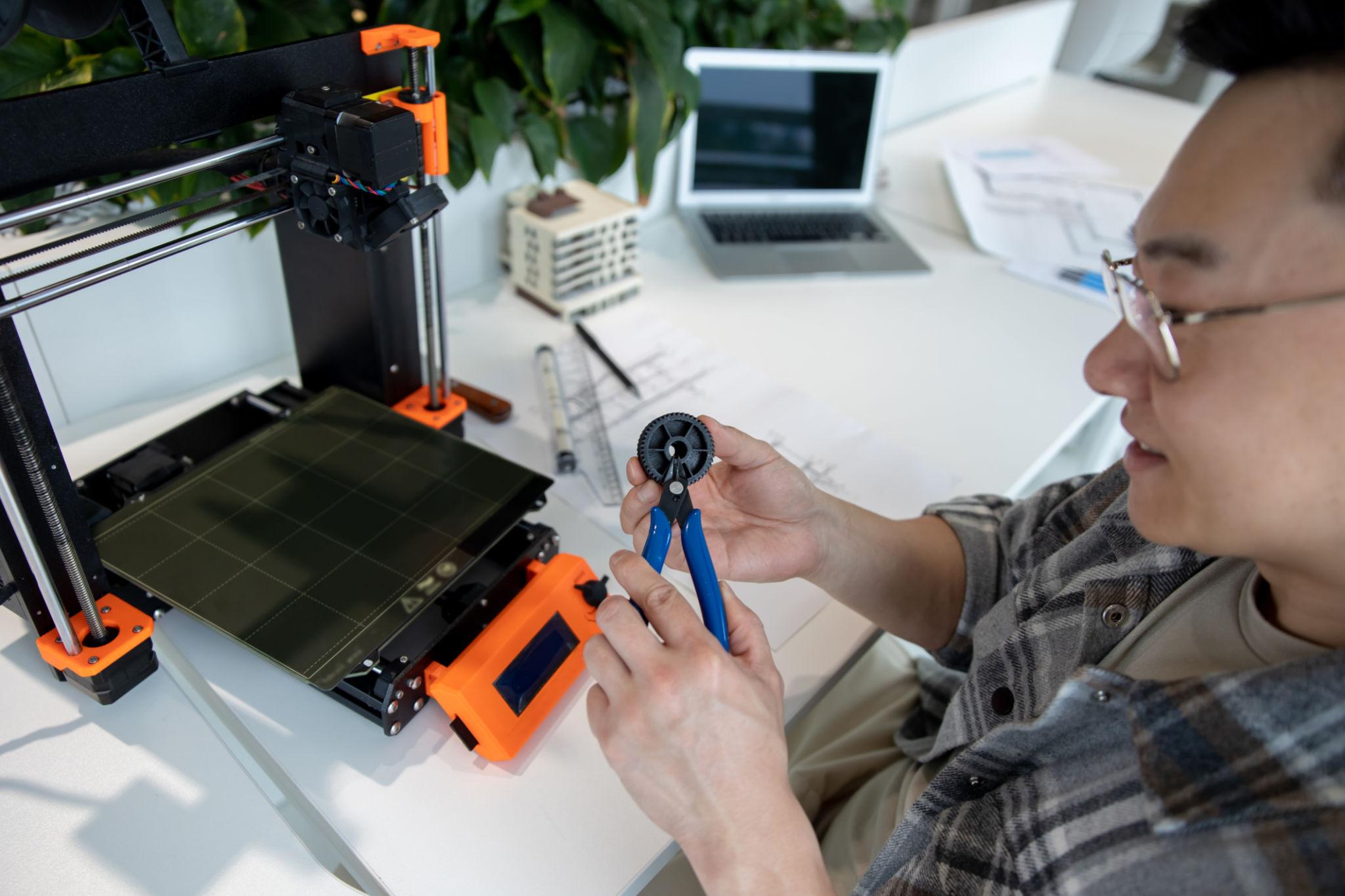 Asian designer engineer using 3D printer in laboratory and studying product prototype.
