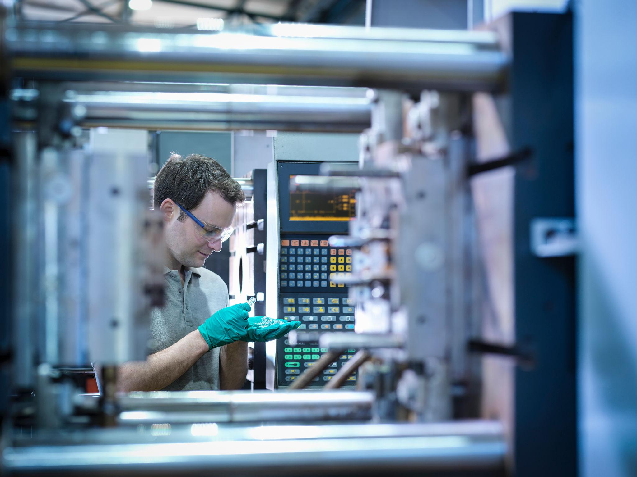 Worker inspecting parts from plastic injection moulding machine in plastics factory.